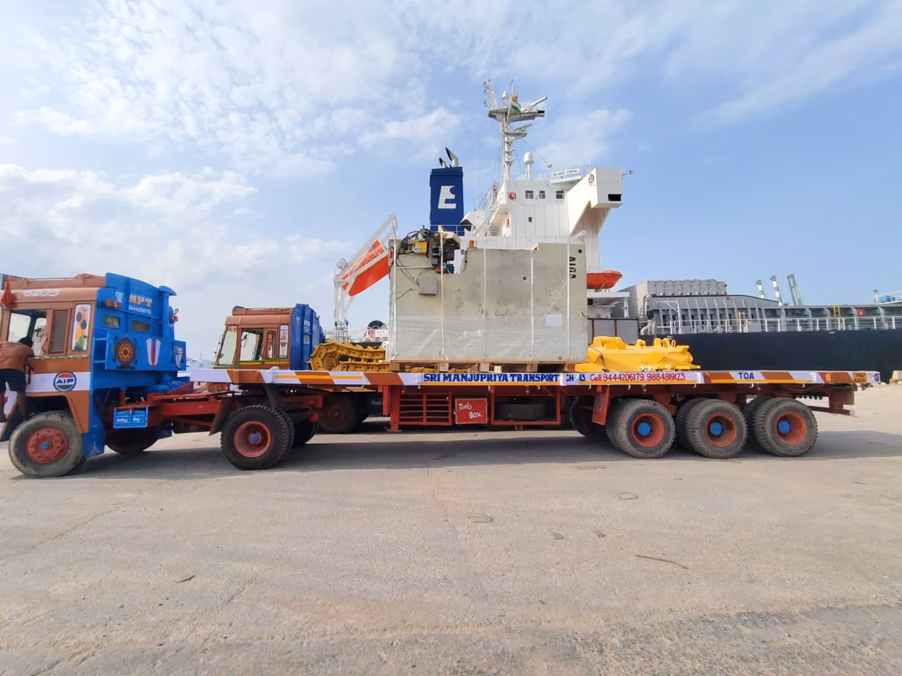 A heavy machine strapped to a low-bed trailer on the quay, with a ship alongside