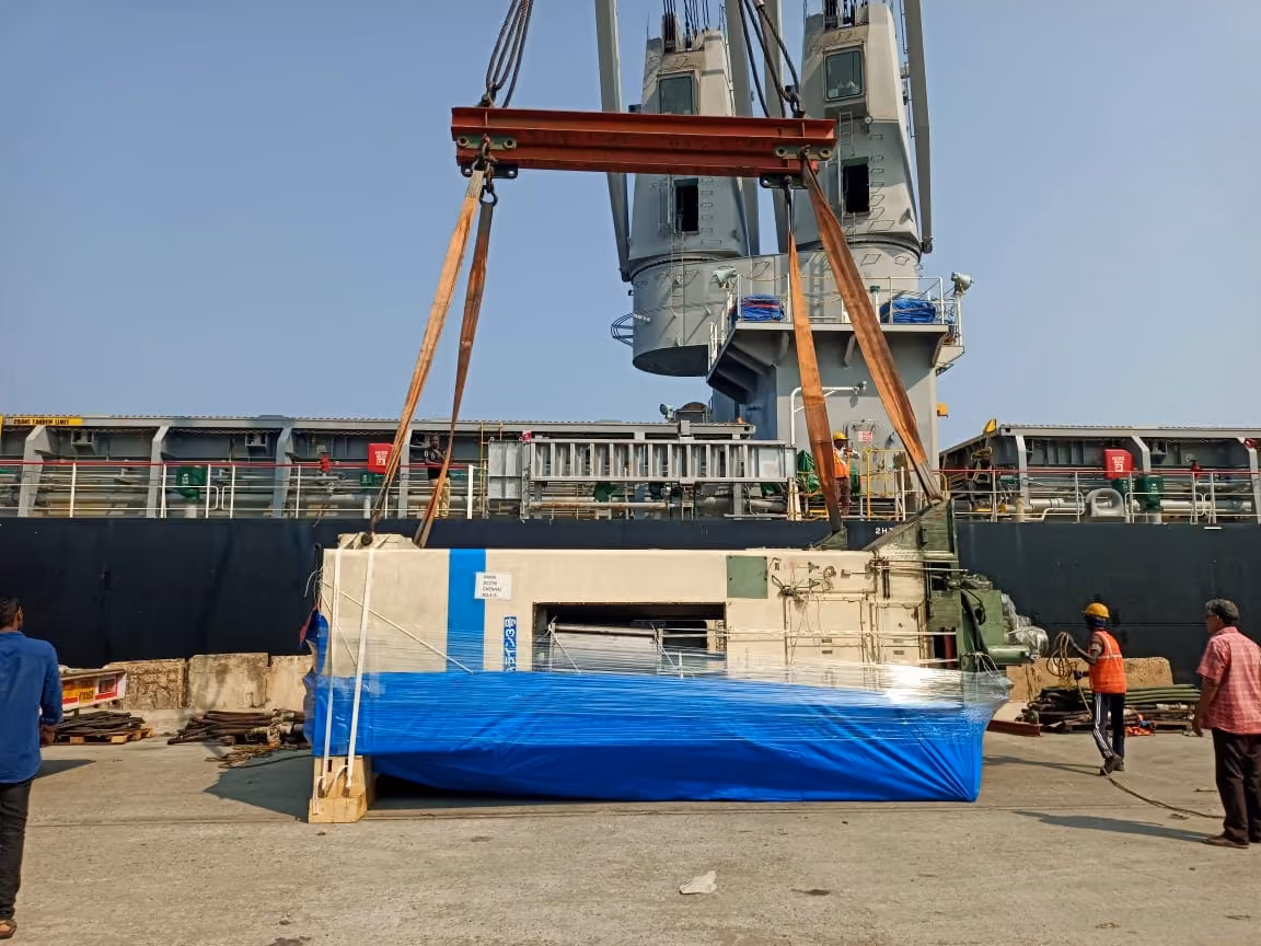 Break-bulk unit in a spreader-beam lift beside a ship’s cranes at the quay