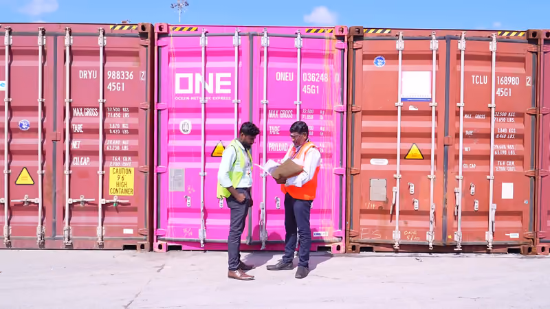 Two Sanguine staff in high-visibility vests reviewing clearance documents in front of stacked containers
