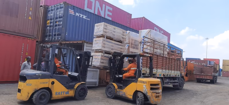 Forklifts loading crated cargo onto a truck between container stacks at the yard