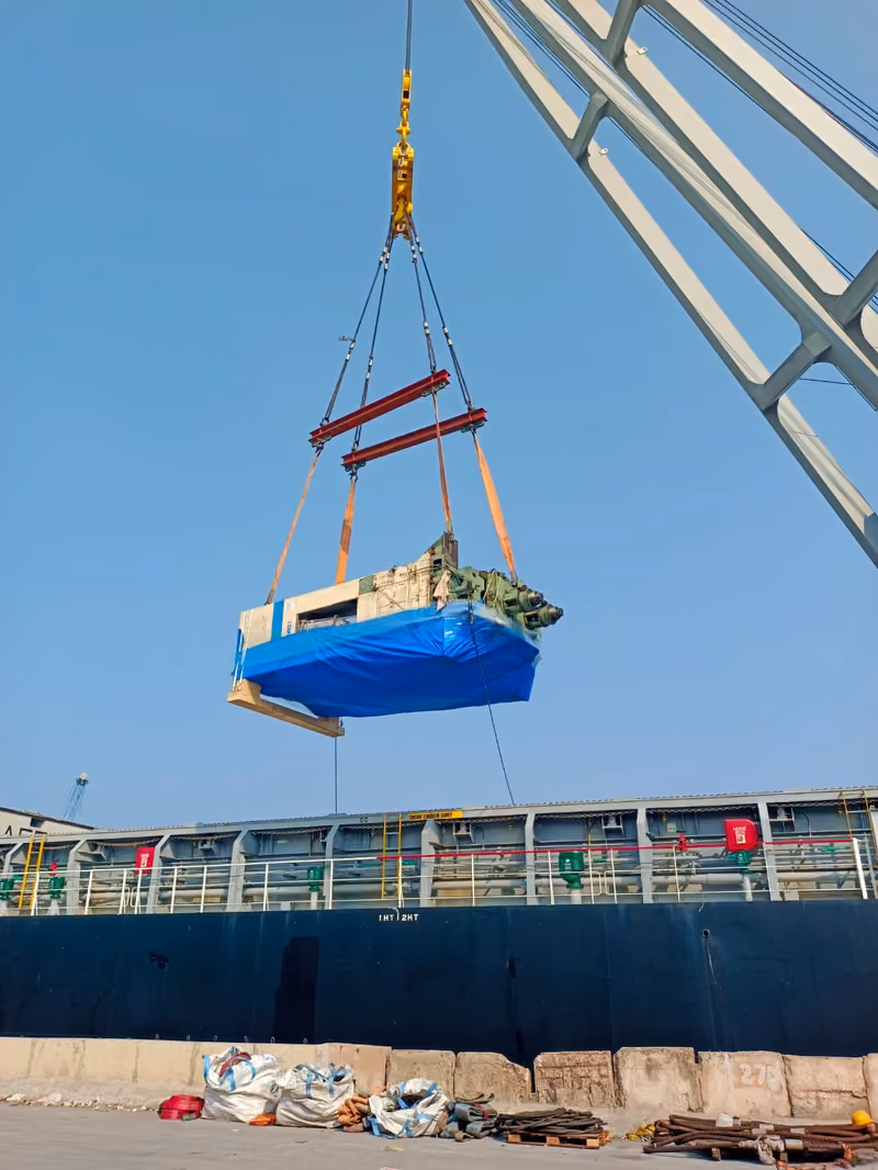 A crated machine in a ship-crane sling above the quay, ready to load